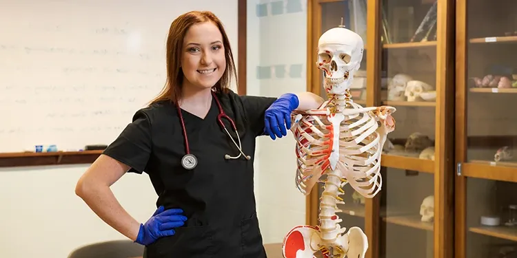 Woman in scrubs with stethoscope next to a skeleton